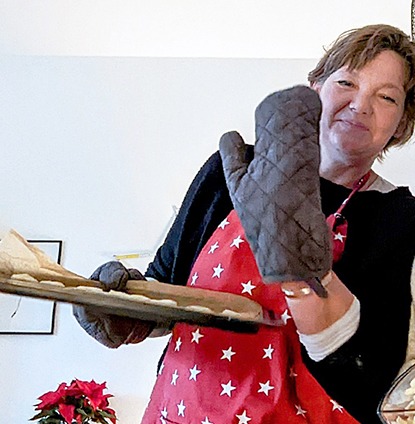 Frau in Weihnachtsbäckerei hält Backblech mit Plätzchen und trägt Schürze – Hinweis auf Gratis PDF „Weihnachtsrezepte mit ätherischen Ölen“ im Shop Geschenke made for Mama.