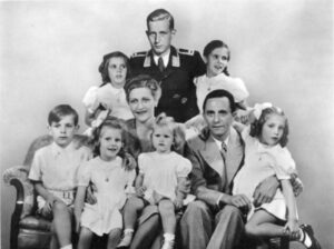 Porträt der Familie Goebbels 1942: Mitte Magda Goebbels, Joseph Goebbels mit ihren sechs Kindern Helga, Hildegard, Helmut, Hedwig, Holdine und Heidrun. Dahinter Harald Quandt in der Uniform eines Feldwebels der Luftwaffe (retuschierte Postkarte)
