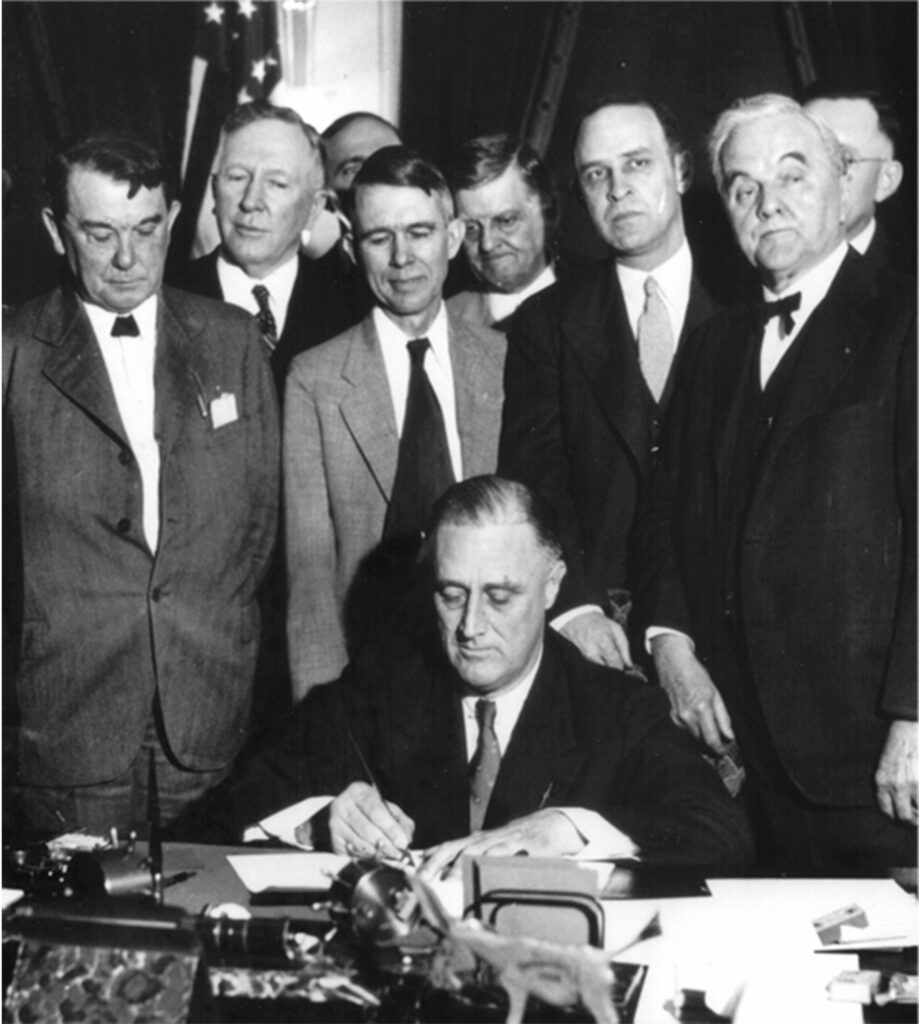 Franklin D. Roosevelt (sitzend) und George W. Norris (vorne rechts) bei der Gründung der Tennessee Valley Authority (1933)